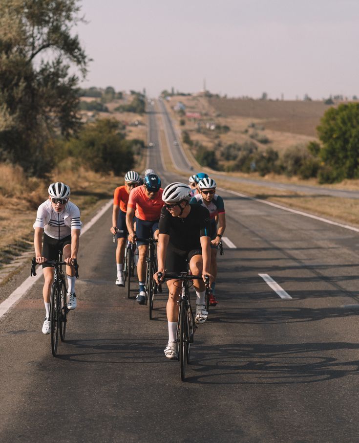 A relaxed group of cyclists riding single file along a tree-lined canal towpath